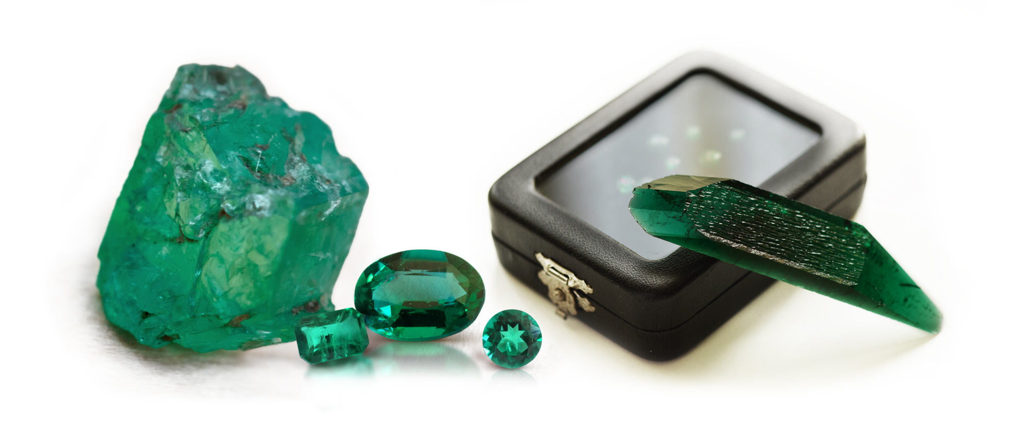 Example of a natural rough emerald crystal, some faceted emerald specimens, as well as one uncut synthetic hydrothermal emerald slab