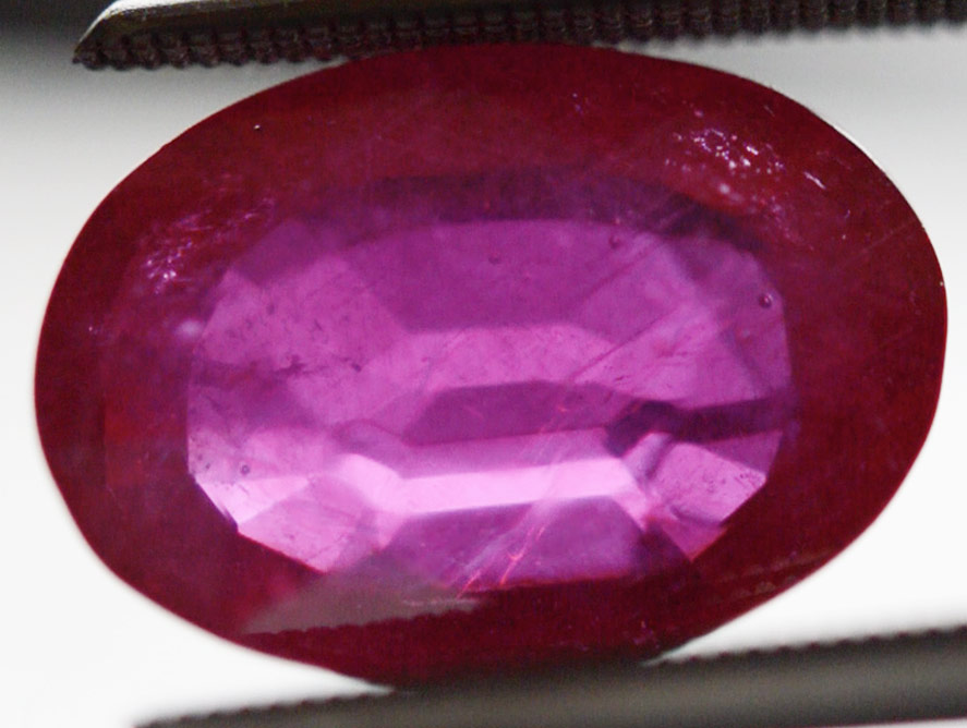 A lead glass fracture-filled natural ruby showing gas bubbles and an orange flash effect