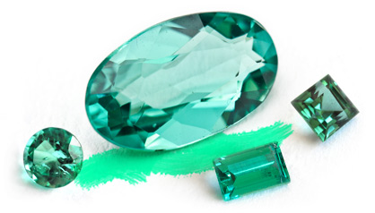 A green faceted gemstone surrounded by smaller emerald specimens