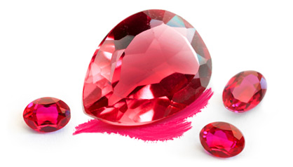 A red faceted gemstone surrounded by smaller ruby specimens