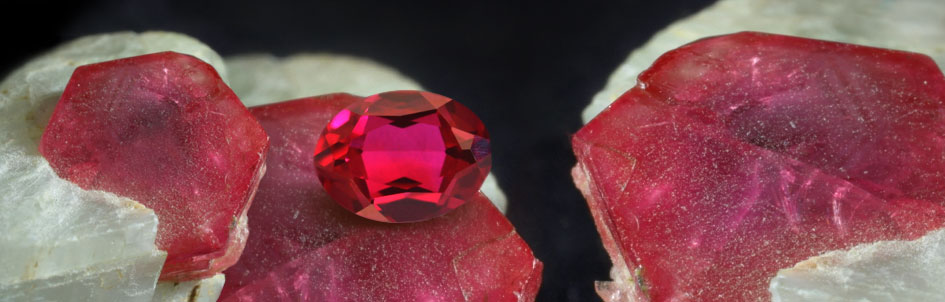 ruby red gemstone on top of a group of rough crystal specimens