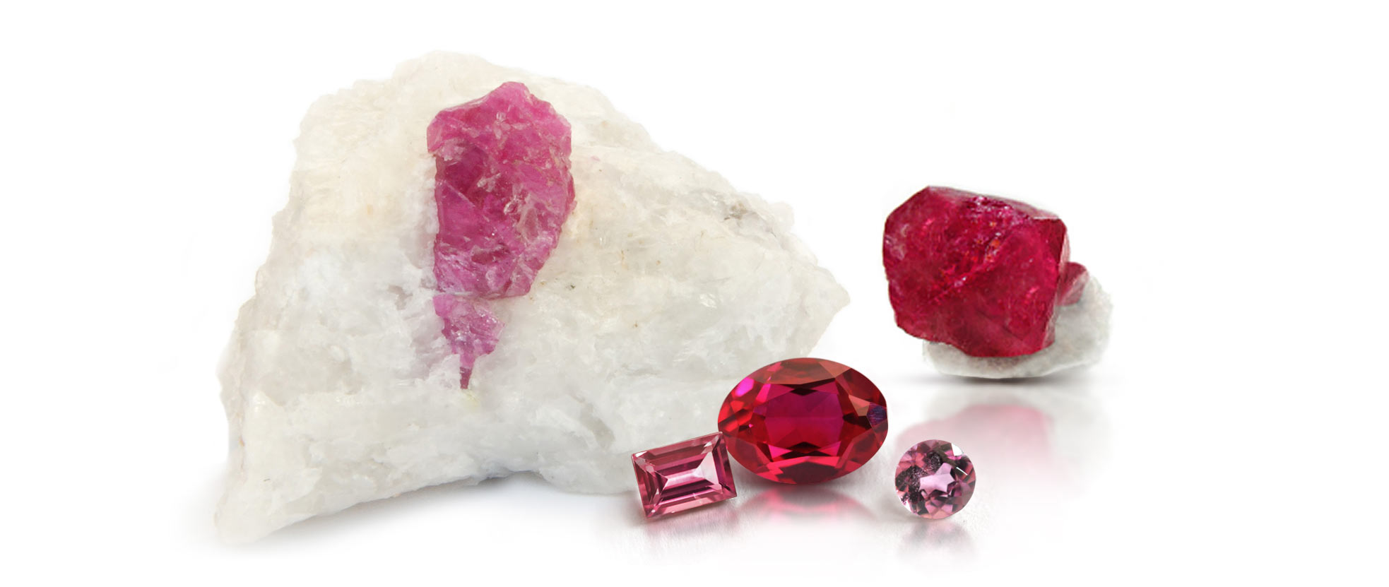 Two examples of rough ruby crystals alongside faceted ruby and pink sapphire gemstones