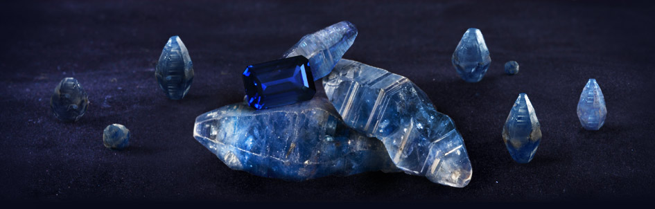 faceted blue sapphire gemstone on top of a group of rough sapphire corundum specimens