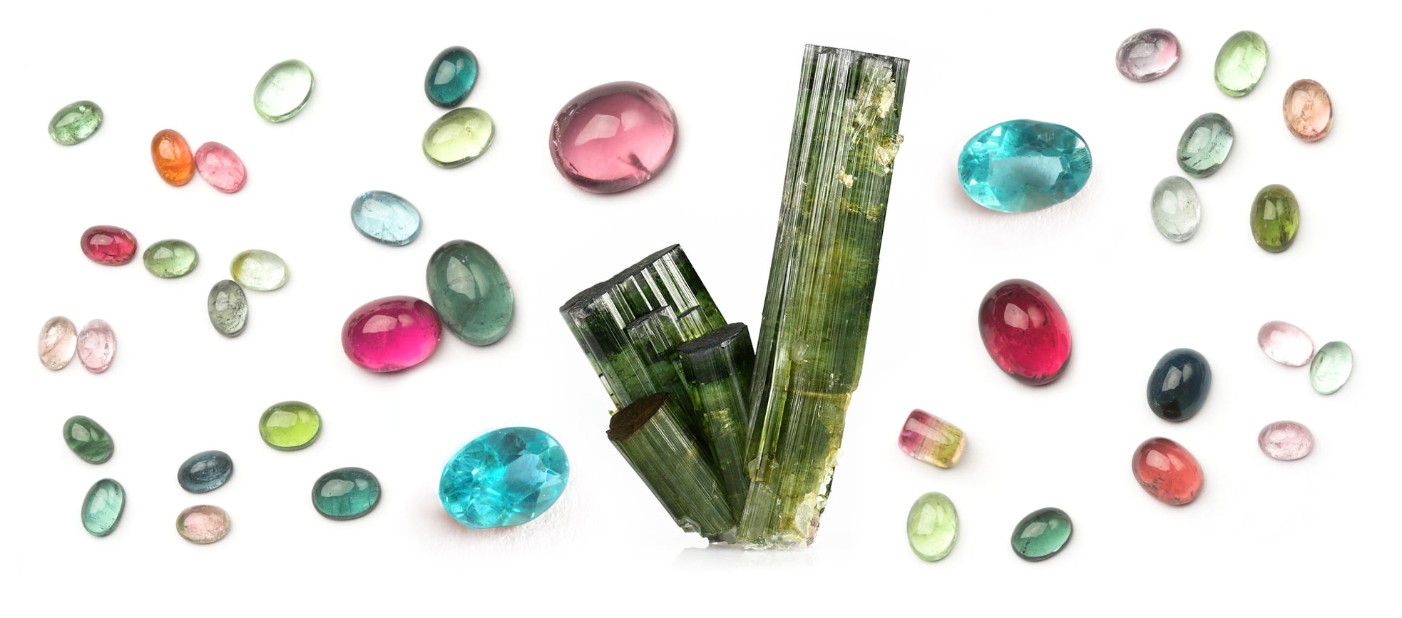 A colorful selection of tourmaline cabochons and faceted stones along with a rough tourmaline crystal